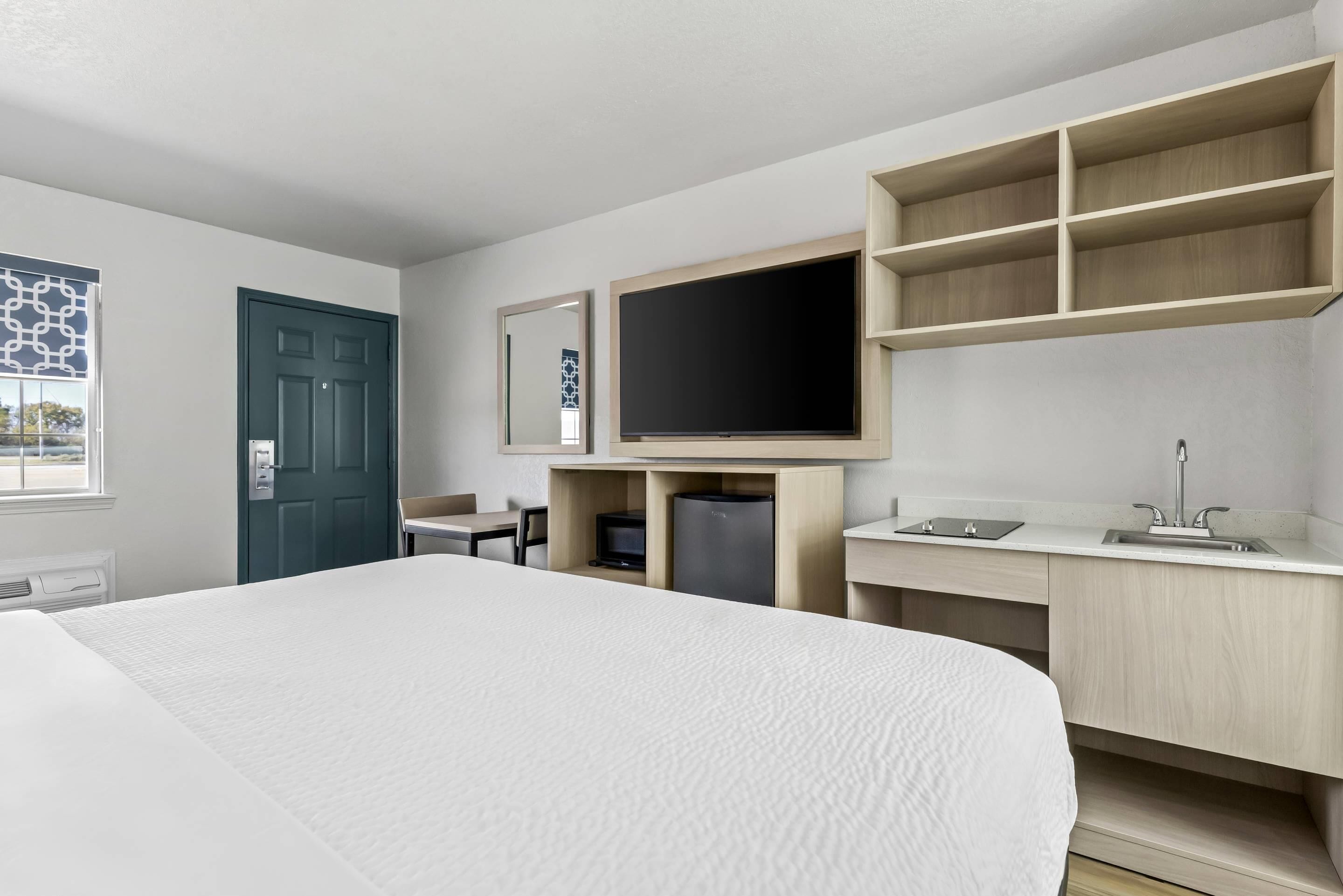 Ein Hotelzimmer mit einem Bett, einem Fernseher, einem Schreibtisch mit Waschbecken und einer Tür.
