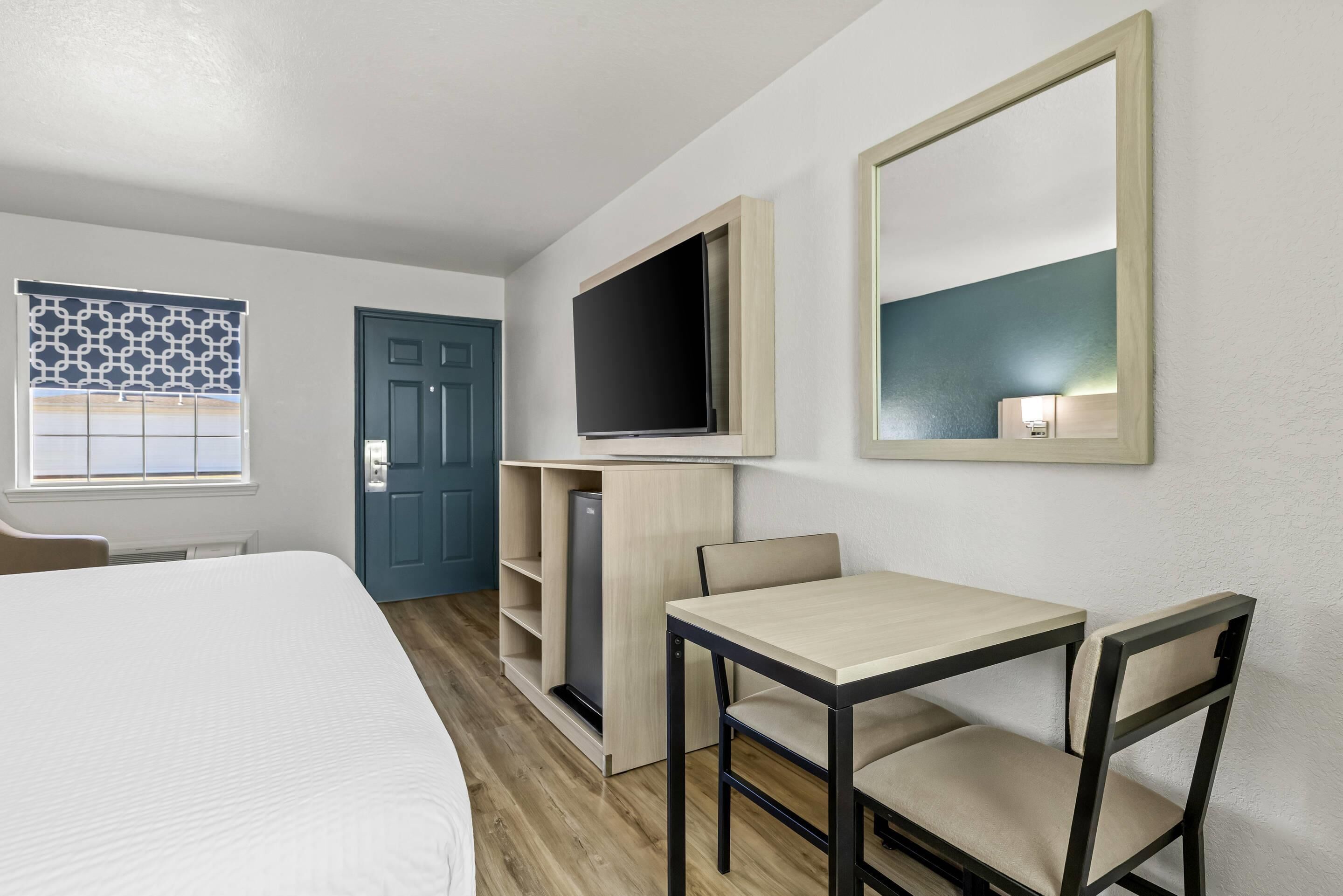 Una habitación de hotel con cama, escritorio con dos sillas, televisión montada en la pared, armario y una puerta.