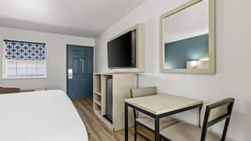 Una habitación de hotel con cama, escritorio con dos sillas, televisión montada en la pared, armario y una puerta.