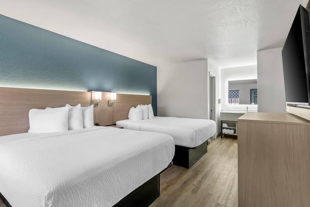 A hotel room with two beds, a desk, and a TV.
