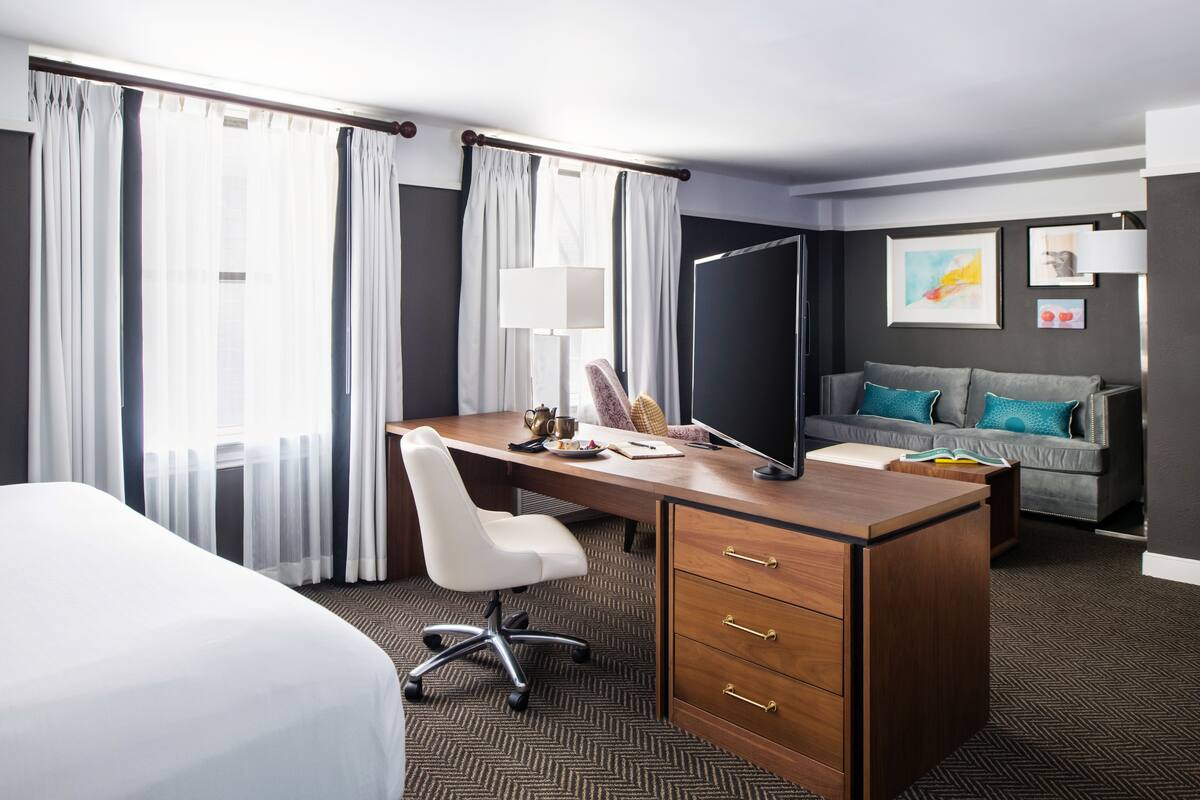 A hotel room with a bed, a desk with a chair, a sofa, and a TV.