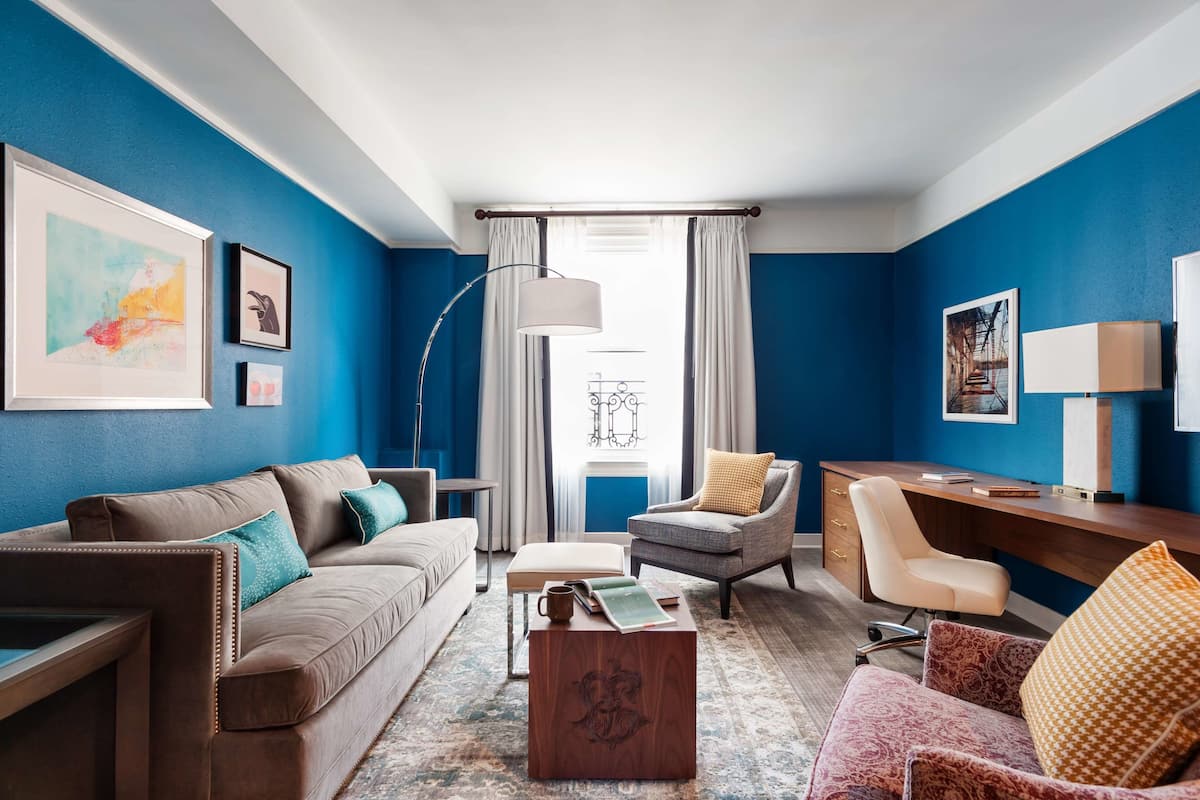 A modern living room with a blue accent wall, a sofa, a chair, a desk, and a coffee table.