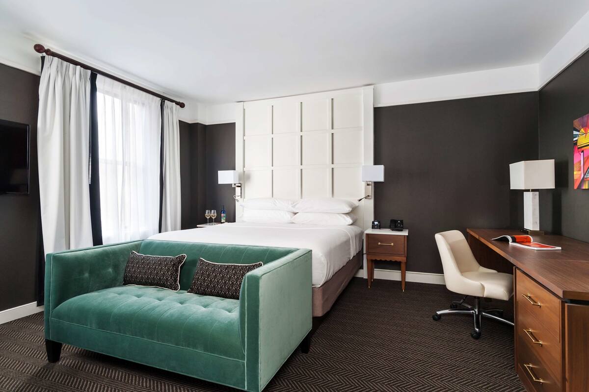 A hotel room with a large bed, a green sofa, a desk, and a chair.