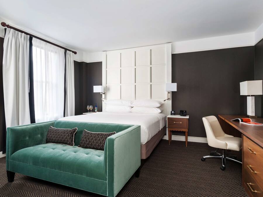 Ein Hotelzimmer mit einem großen Bett, einem grünen Sofa, einem Schreibtisch und einem Sessel.
