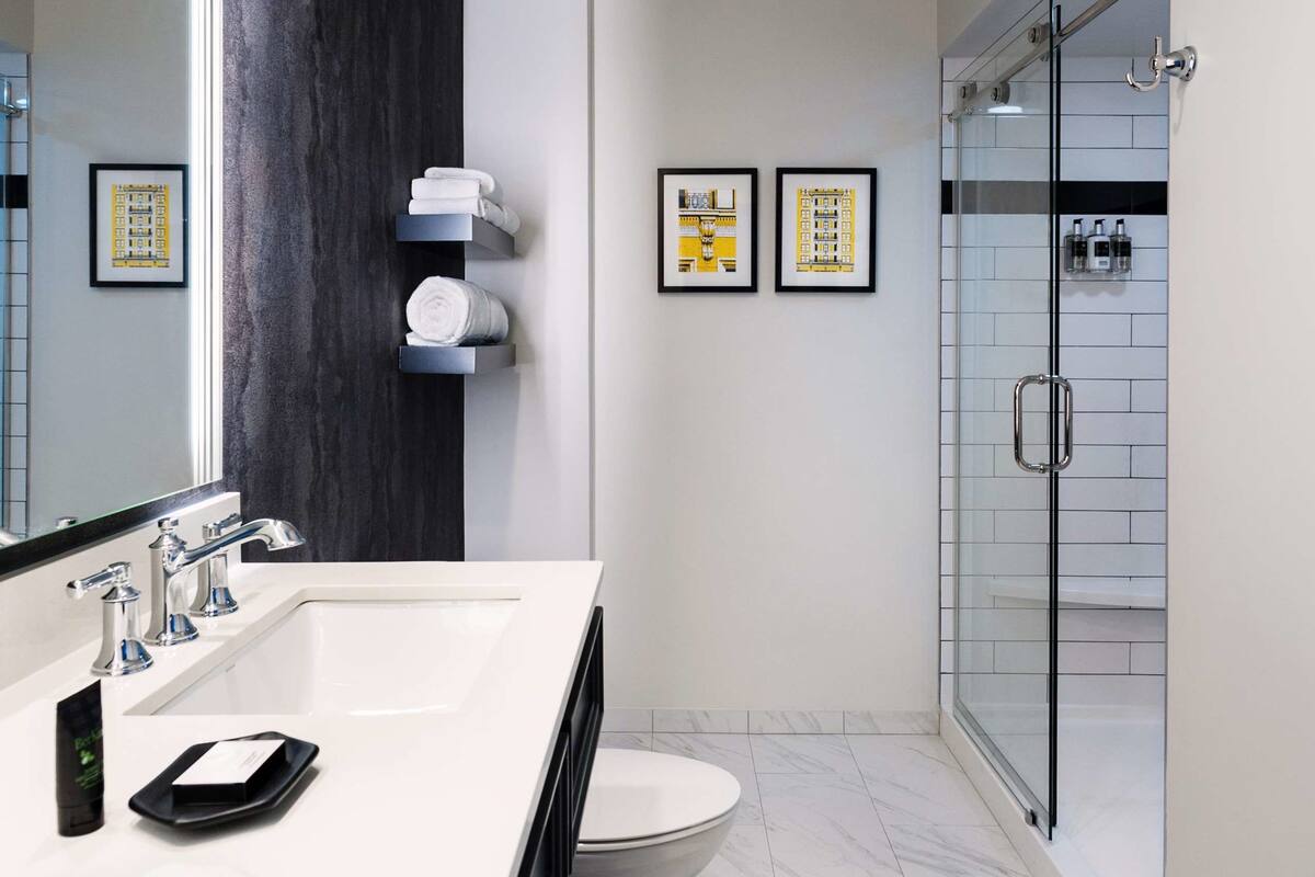 A modern bathroom with a large mirror, white sink, and a glass-enclosed shower.