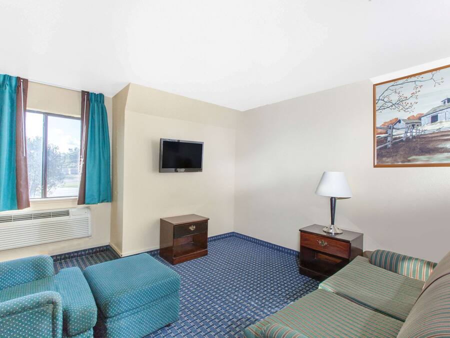 A hotel room with a bed, a sofa, a TV, a lamp, and a painting on the wall.
