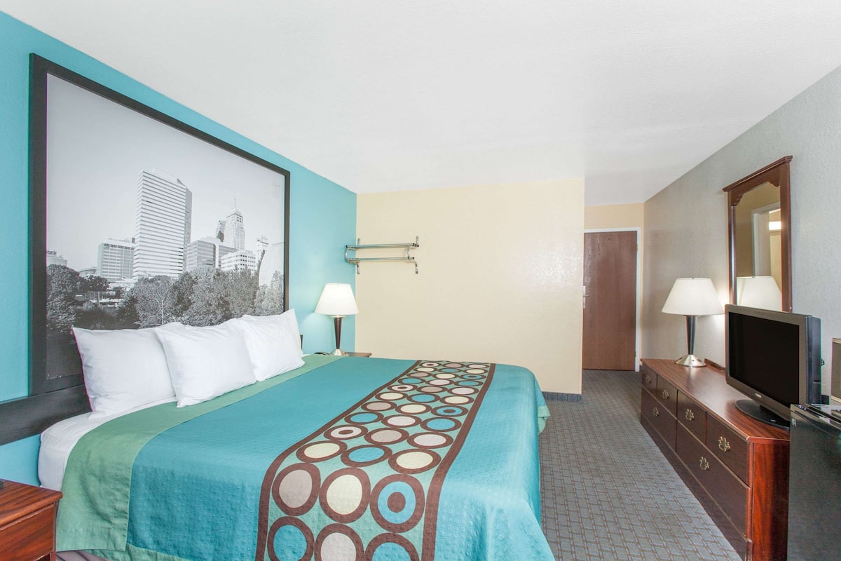 A hotel room with a bed, a television, a dresser, and a cityscape painting on the wall.
