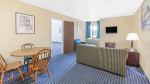 A hotel room with a dining table, chairs, a sofa, a TV, and a lamp. - Super 8 by Wyndham Sallisaw (Sallisaw)