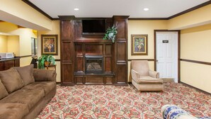 A hotel lobby with a fireplace, a sofa, a chair, and a patterned carpet. - Super 8 by Wyndham Sallisaw (Sallisaw)