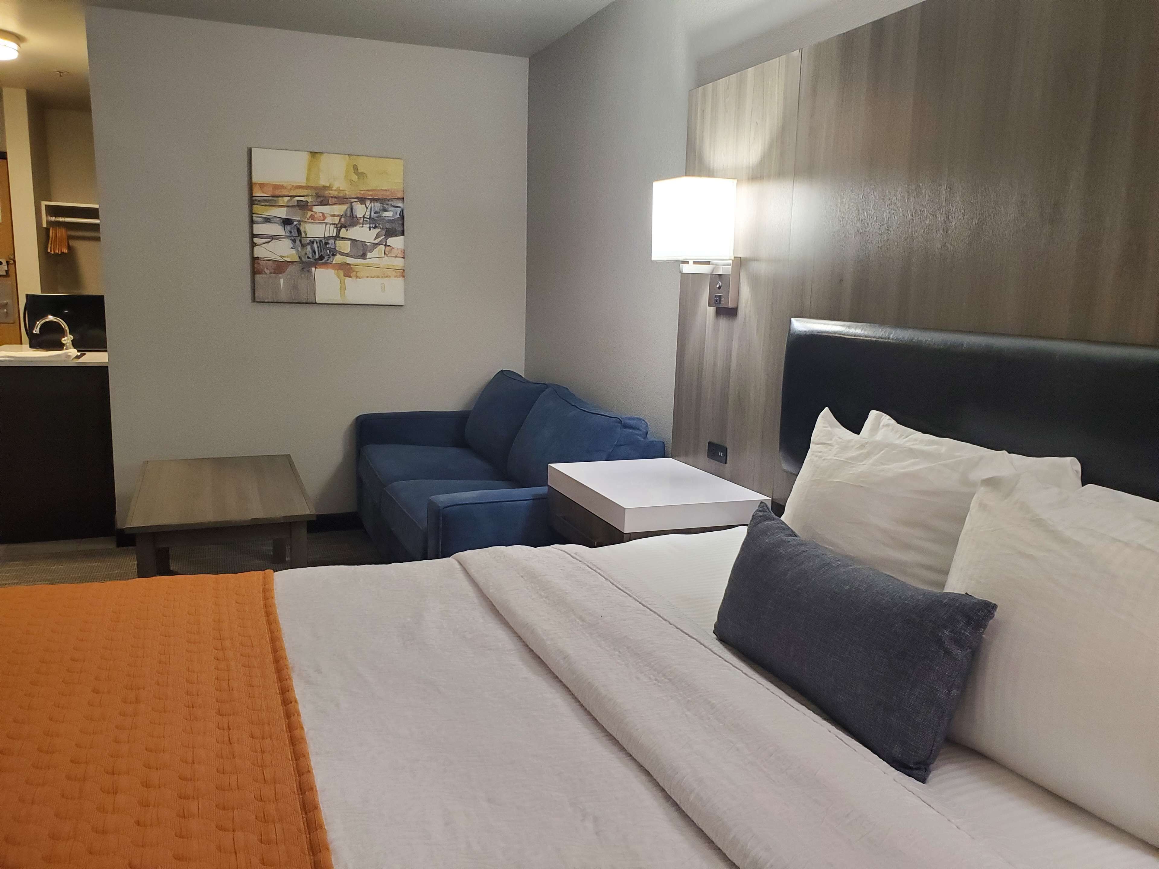 A hotel room with a bed, a desk, a chair, a lamp, and a painting on the wall.