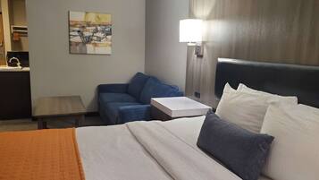 A hotel room with a bed, a desk, a chair, a lamp, and a painting on the wall.