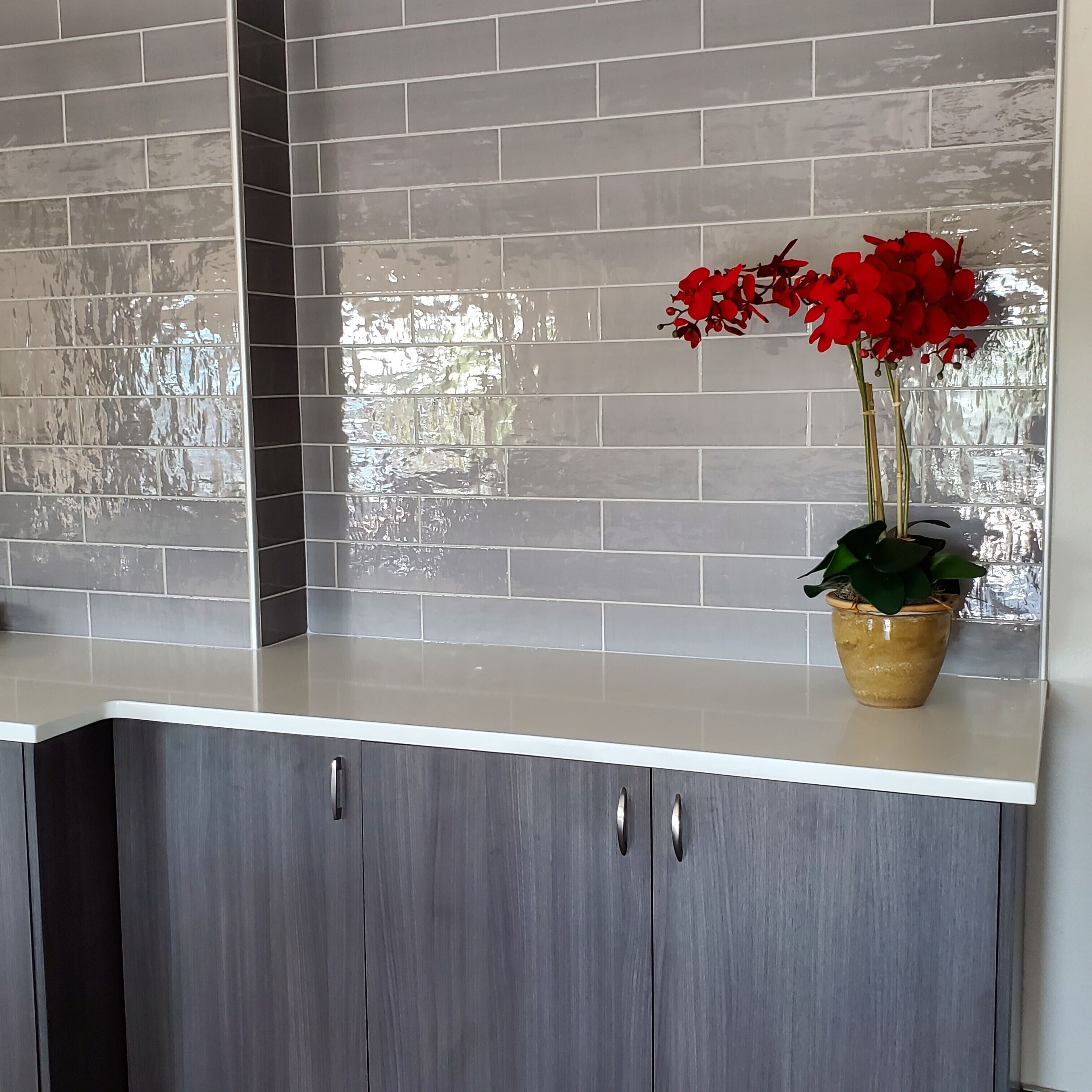 A kitchen with grey cabinets, a white countertop, and a tiled backsplash.