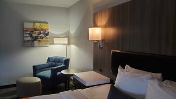 A hotel room with a bed, a desk, a chair, a lamp, and a painting on the wall.