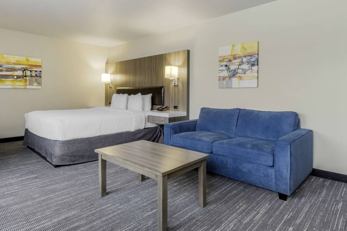 A hotel room with a bed, a blue sofa, a small table, and two wall-mounted lamps.