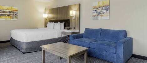 A hotel room with a bed, a blue sofa, a small table, and two wall-mounted lamps.