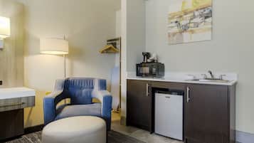 Camera d'albergo compatta con angolo cottura, una poltrona blu, un piccolo frigorifero, un forno a microonde e un attaccapanni.