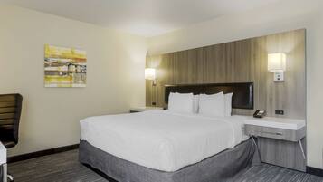 Une chambre d’hôtel avec un grand lit, un bureau avec une chaise, une table de chevet, une lampe fixée au mur et un tableau accroché au mur.