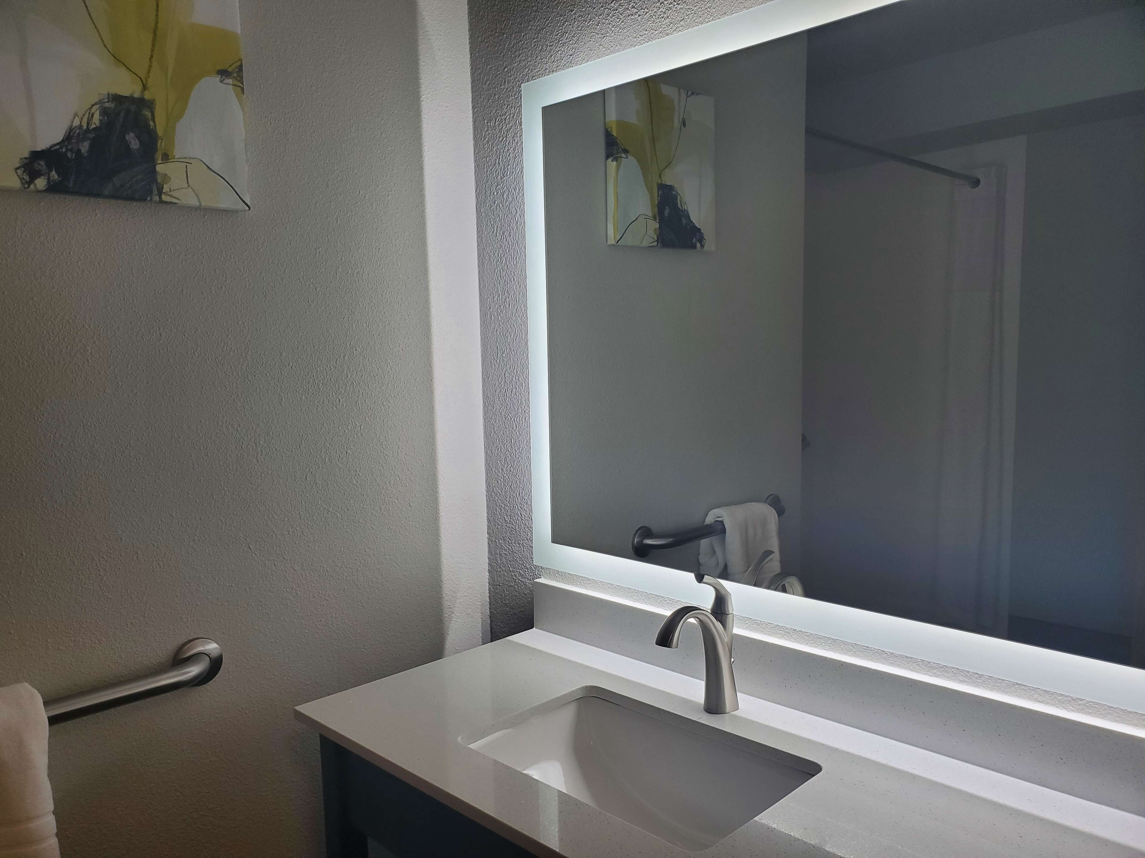 Un baño con un espejo grande, un lavabo y un perchero para toallas.