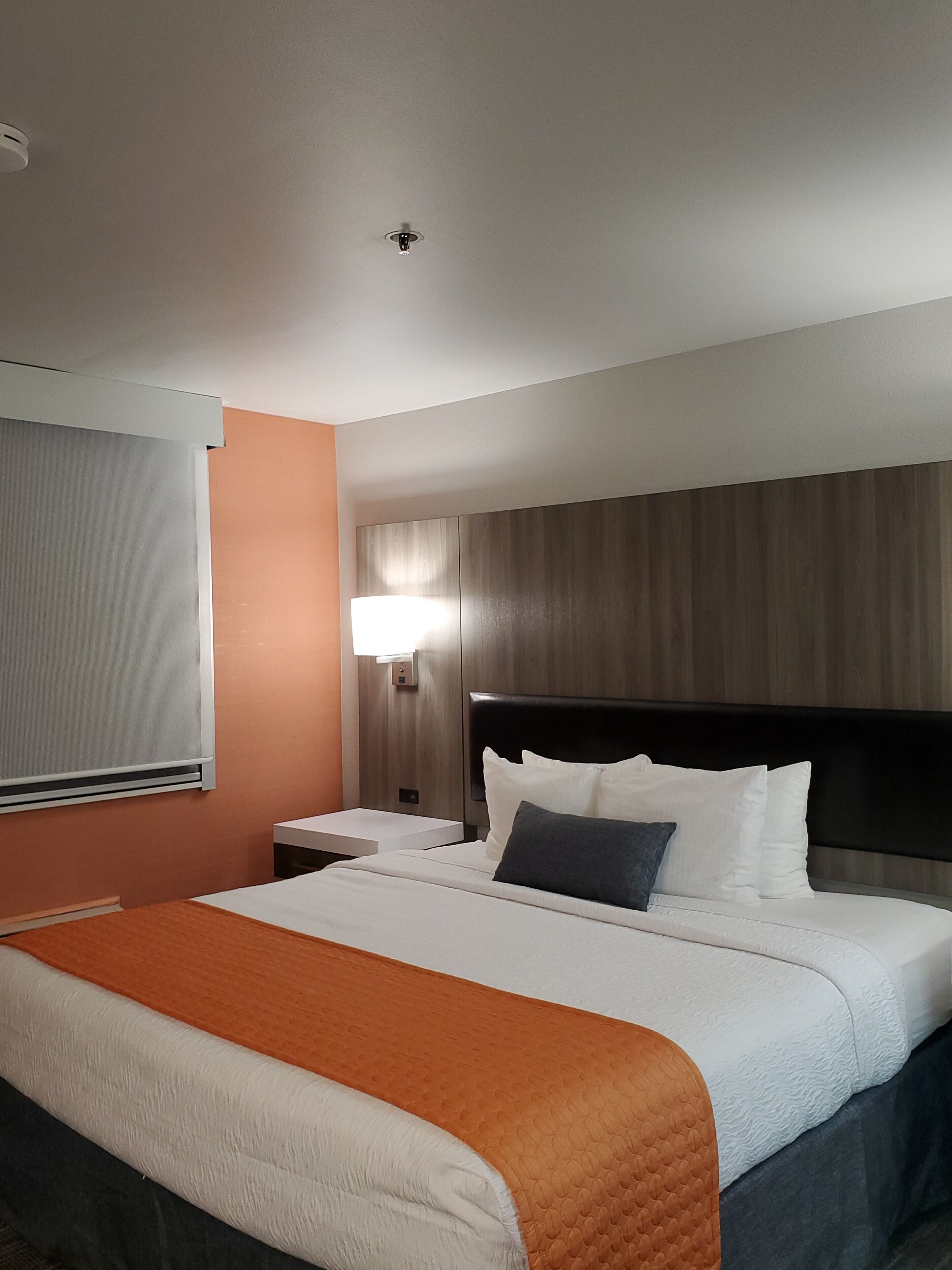 A hotel room with a bed, a nightstand, a lamp, and a window with blinds.