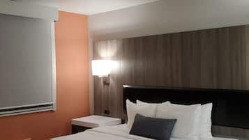 A hotel room with a bed, a nightstand, a lamp, and a window with blinds.