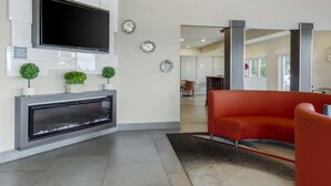 A modern living area with a flat-screen TV, a fireplace, and a red sofa. - Best Western Plus Renton Inn (Renton)