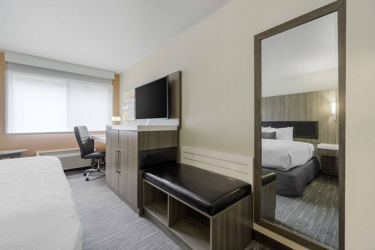 A hotel room with a bed, a desk, a chair, a TV, and a mirror.