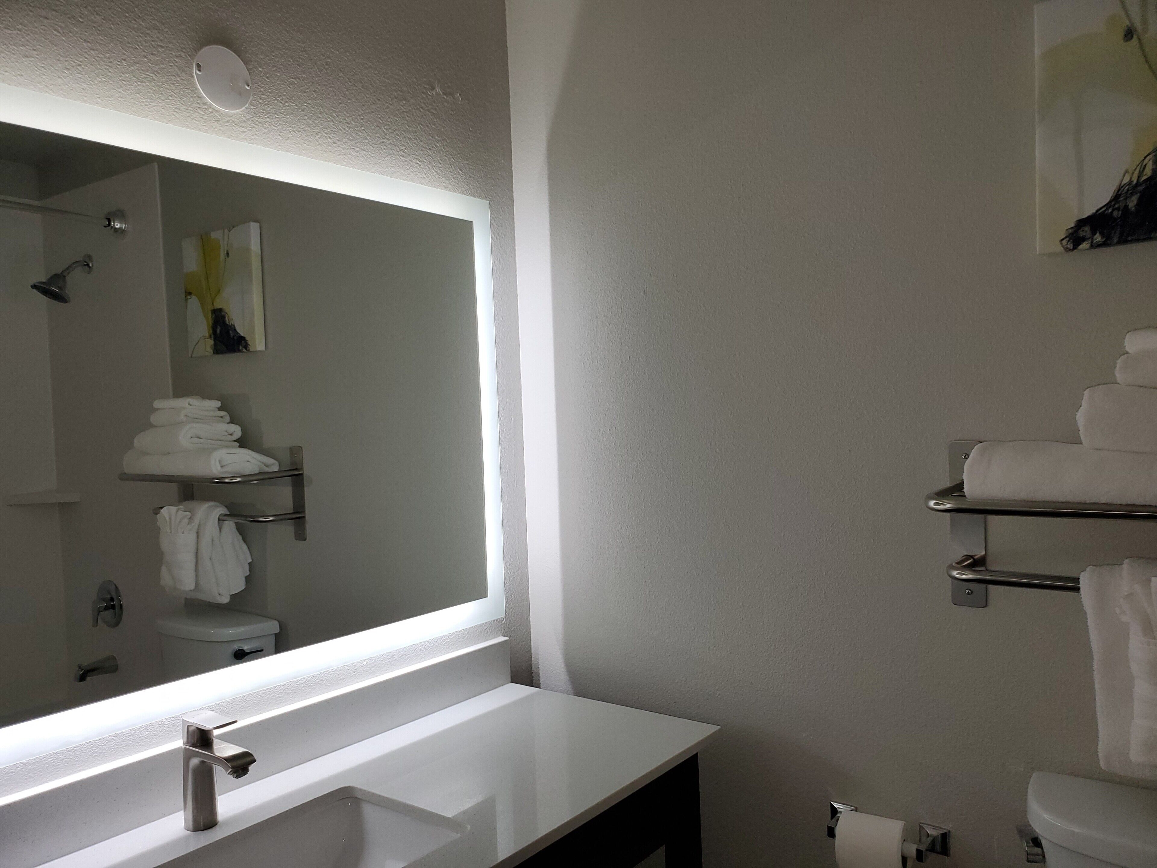 A modern bathroom with a large mirror, white sink, and towel racks.