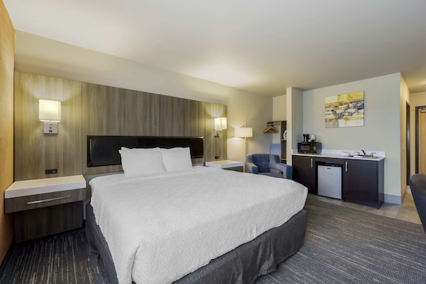 A hotel room with a large bed, bedside tables, a desk with a microwave, and a chair.