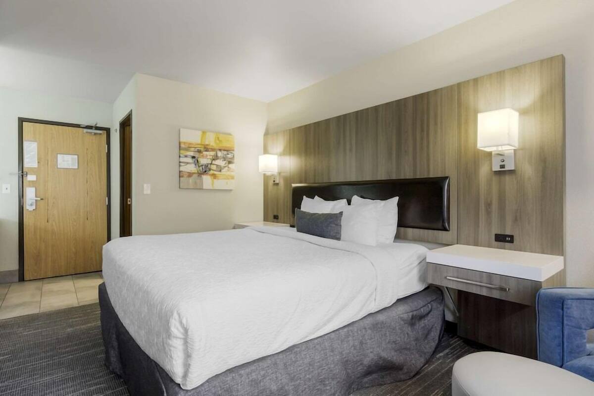 A hotel room with a large bed, a bedside table, a chair, a wooden headboard, and two wall-mounted lamps.