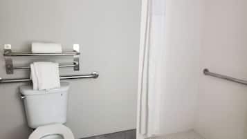 Un baño con inodoro, toallero con toallas, cortina de ducha y barra de apoyo.