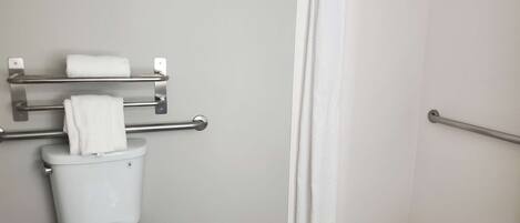 Een badkamer met toilet, een handdoekrek met handdoeken, een douchegordijn en een greep.