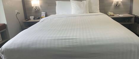 A neatly made bed with white linens, a bedside table with a lamp, a phone, and a sign on the wall.
