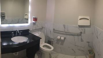 A bathroom with a marble-tiled wall, a black sink, a white toilet, and a handrail.