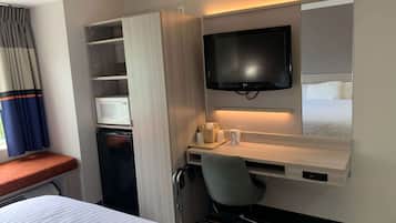 Quarto de hotel com cama, escrivaninha com cadeira, televisão, micro-ondas e guarda-roupa.