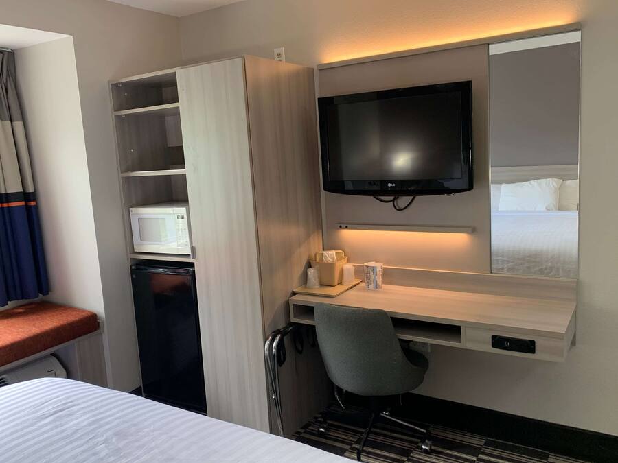 Quarto de hotel com cama, escrivaninha com cadeira, televisão, micro-ondas e guarda-roupa.