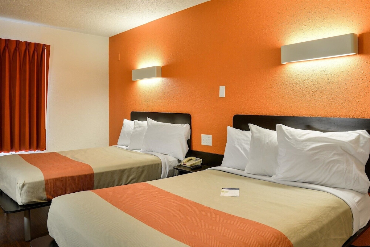 A hotel room with two beds, orange walls, and a curtain.