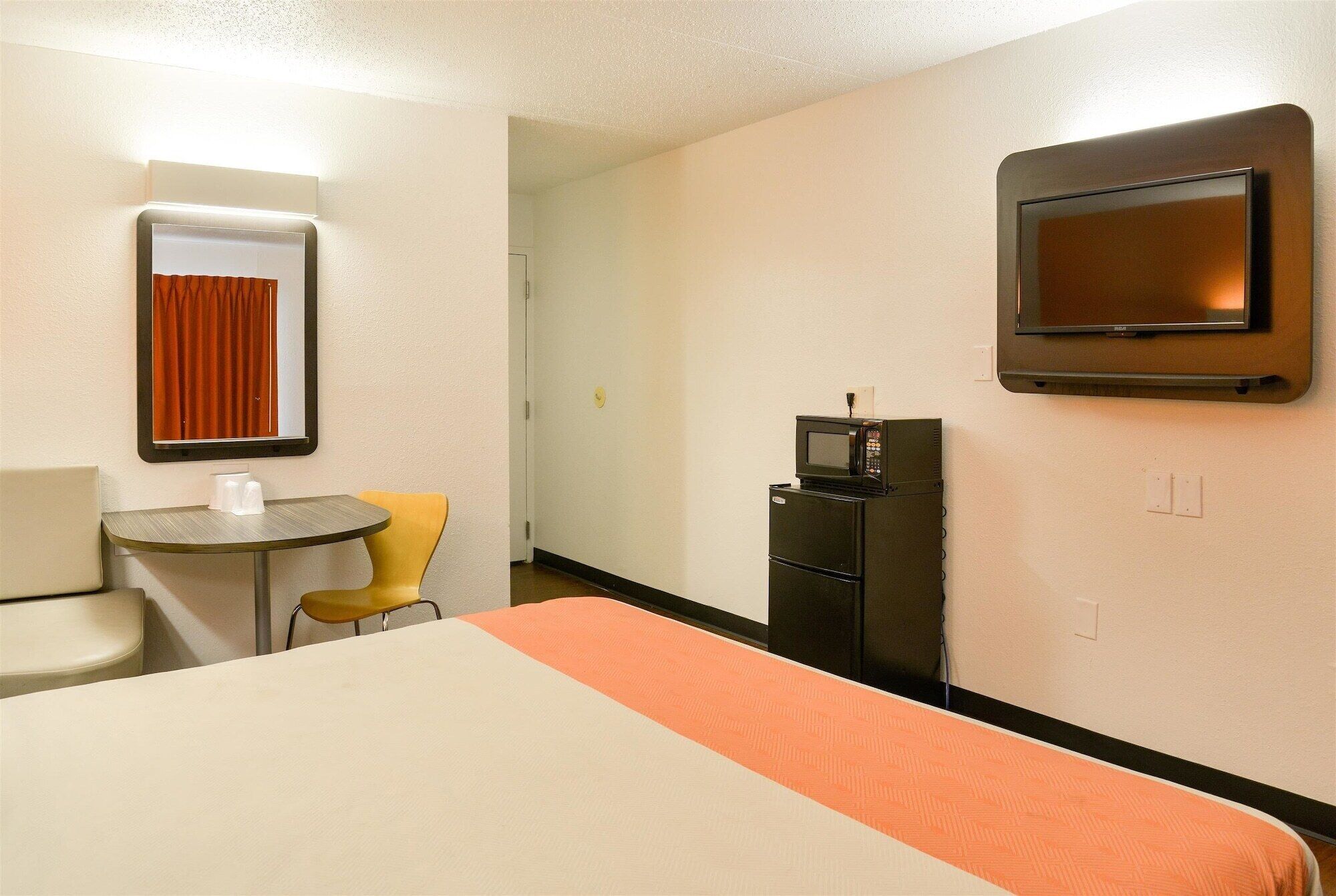 Ein Hotelzimmer mit einem Bett, einem kleinen Tisch mit zwei Stühlen, einer Mikrowelle, einem Fernseher und einer Tür zu einem weiteren Zimmer.