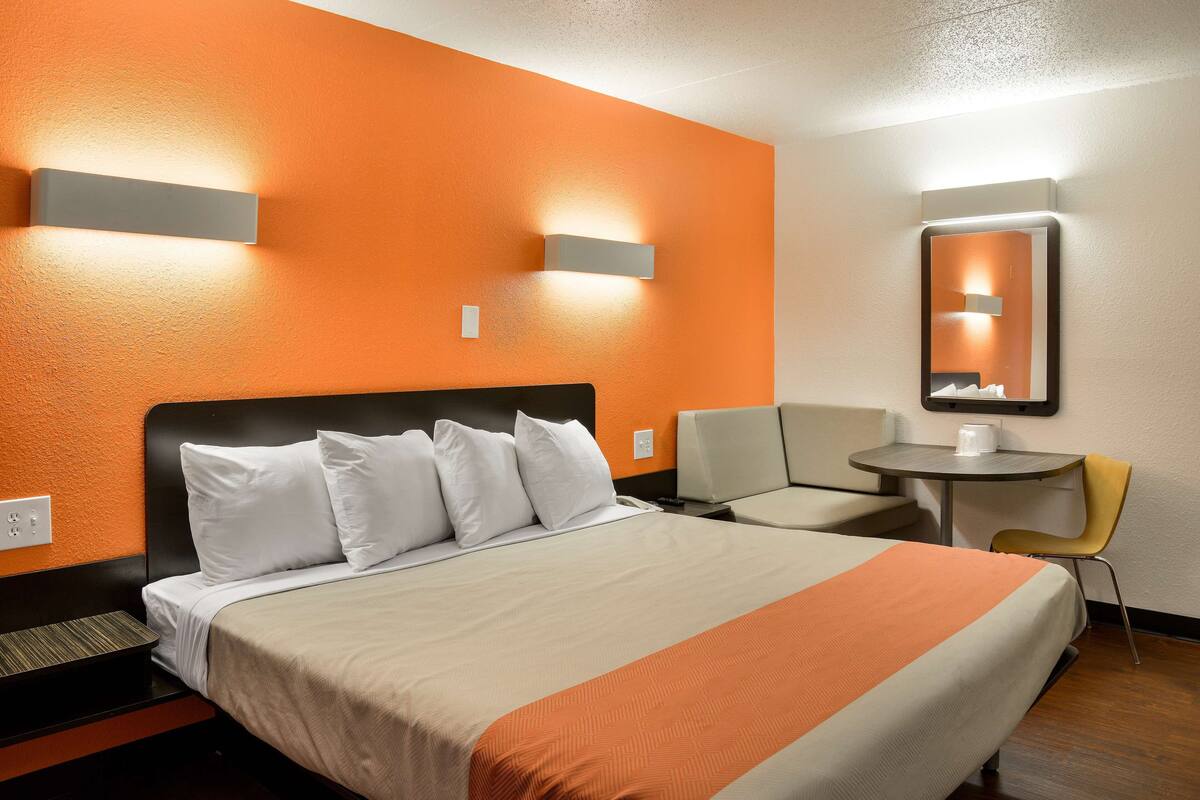 A hotel room with a large bed, a small table, a chair, and a mirror.