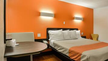A hotel room with a bed, bedside table, chair, and two wall-mounted lights.