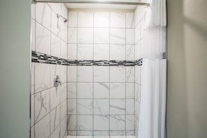 A shower with white marble tiles and a black and white mosaic border. - Travelodge by Wyndham Wahpeton Event Center (Wahpeton)