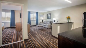 Une chambre d’hôtel avec un tapis à rayures, un canapé, une petite table, une télévision et un coin cuisine.