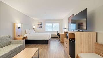 A hotel room with a bed, a desk, a television, a sofa, and a window with a view of trees.
