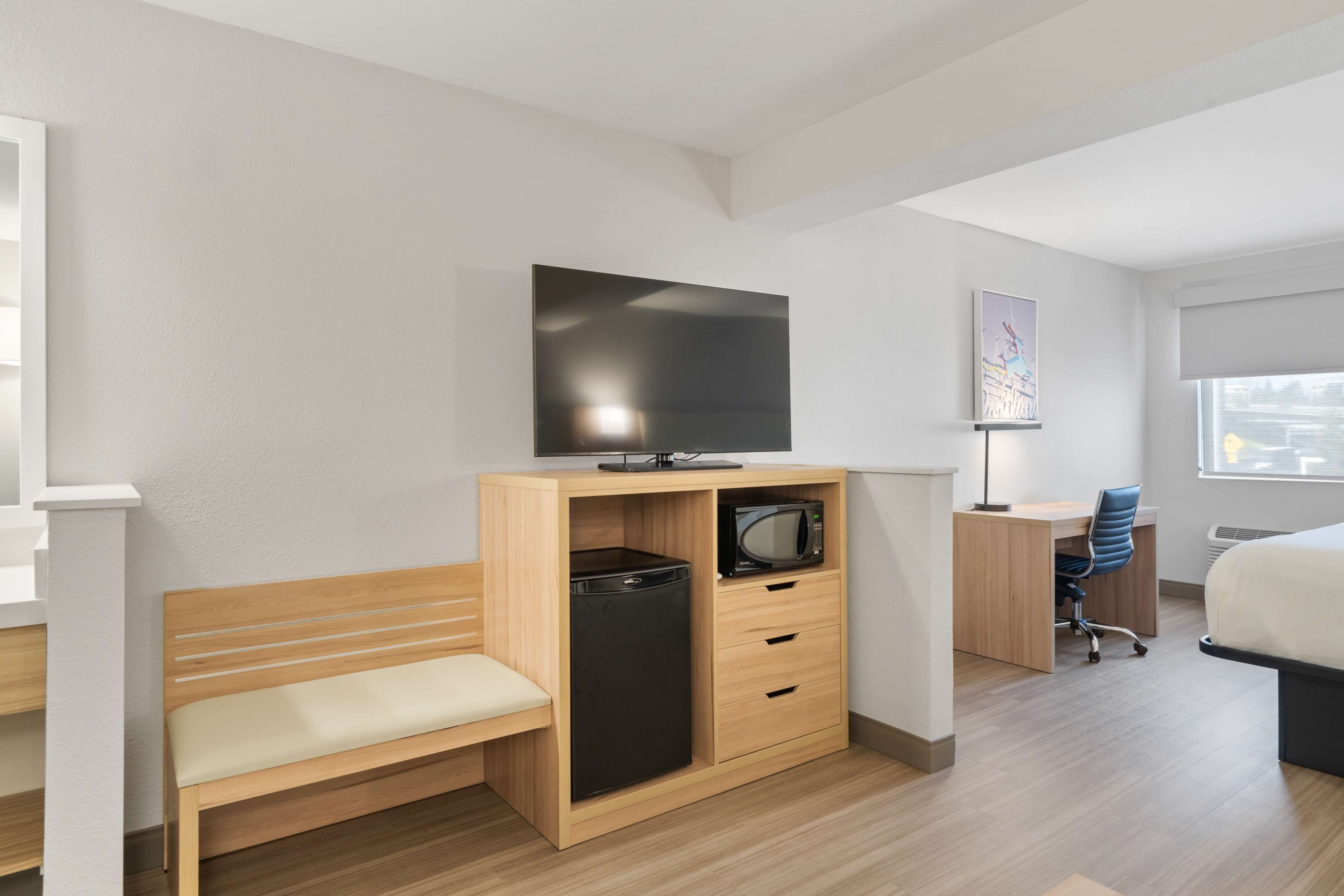 Ein Hotelzimmer mit einer Holzbank, einem Schreibtisch mit Stuhl, einem Fernseher und einer Mikrowelle.