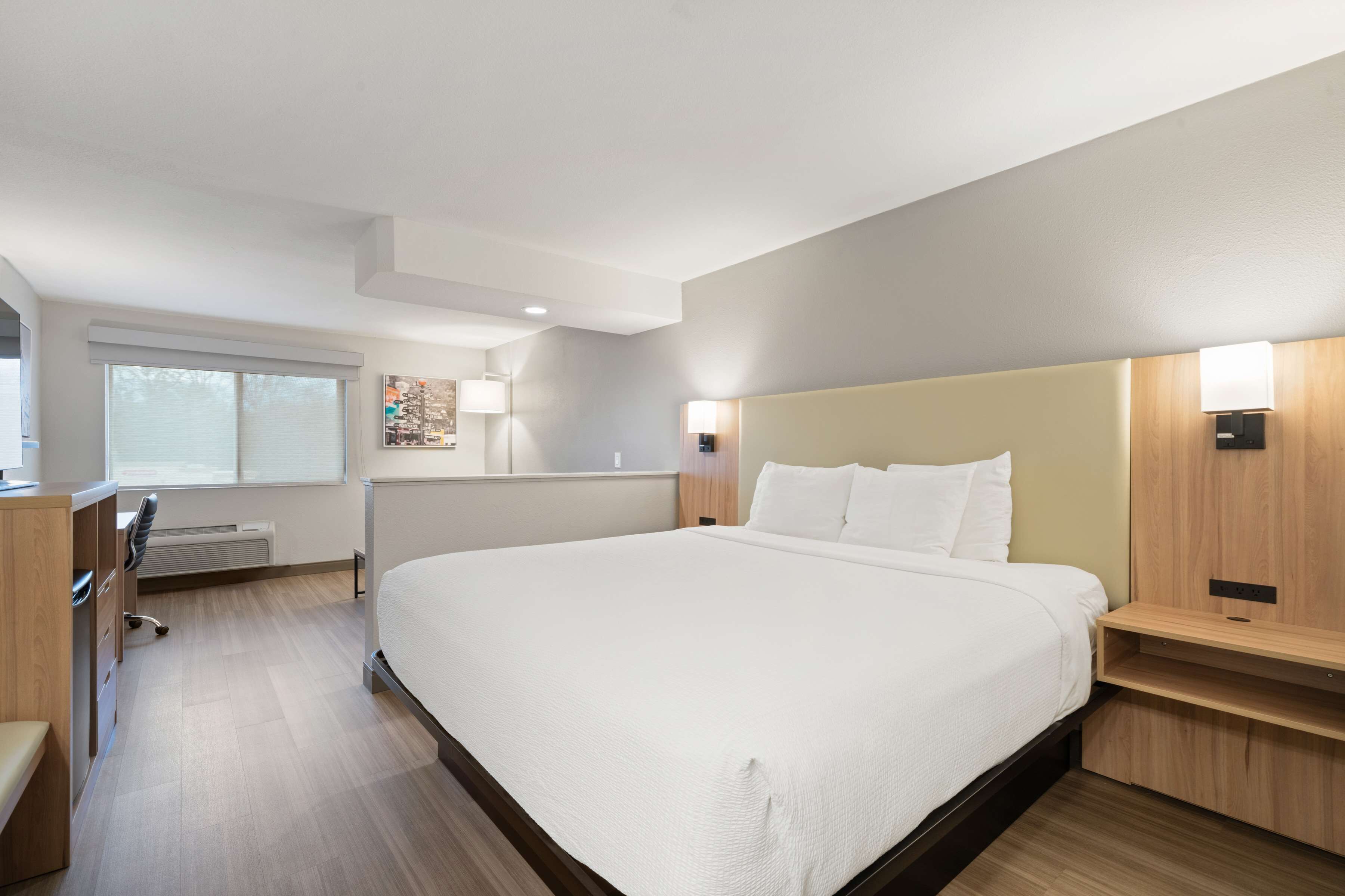 A modern hotel room with a large bed, bedside tables, a desk, and a chair.
