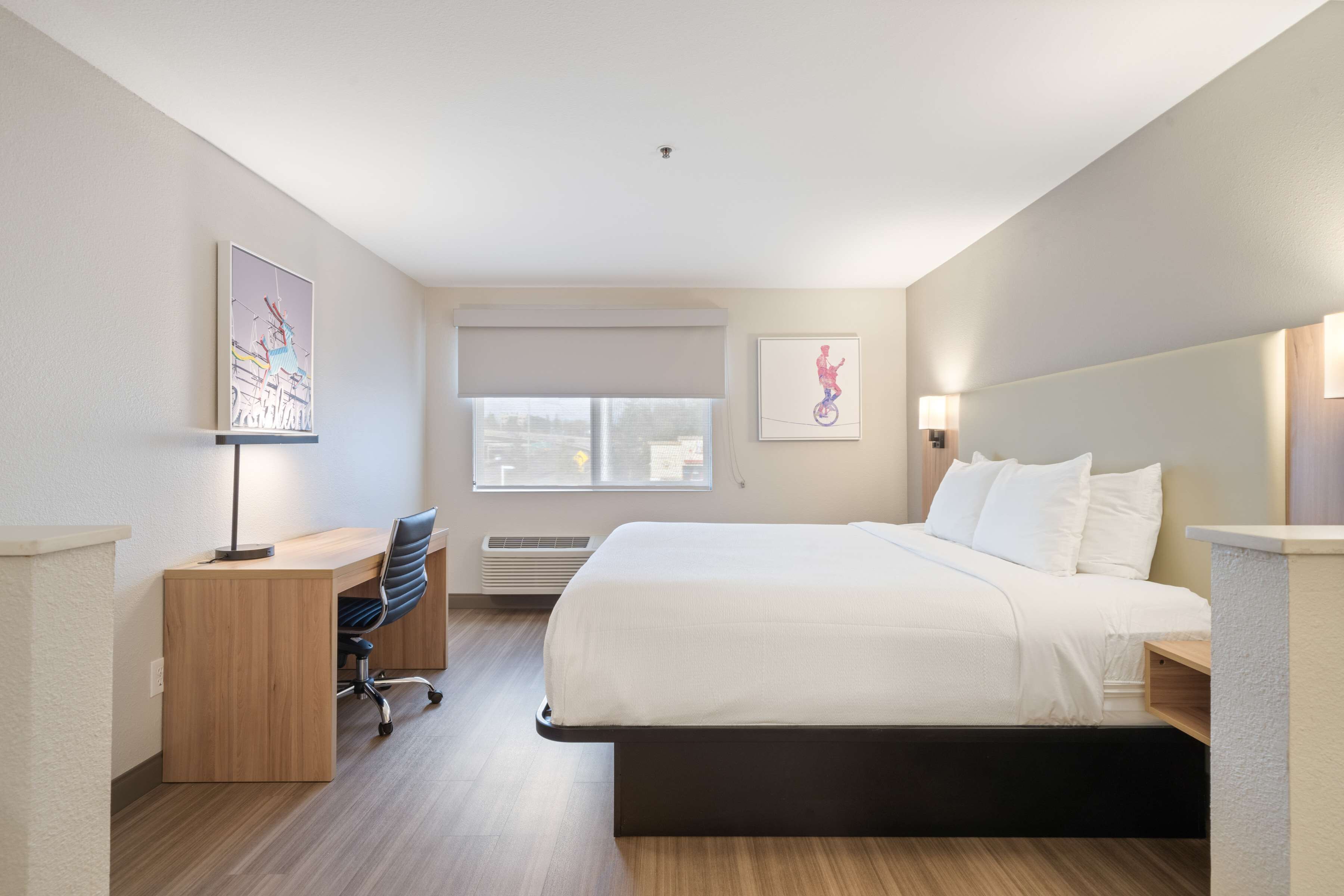 A hotel room with a bed, desk, chair, and artwork on the walls.