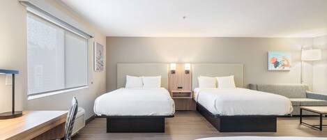 A hotel room with two beds, a desk, a chair, a sofa, and a window with blinds.