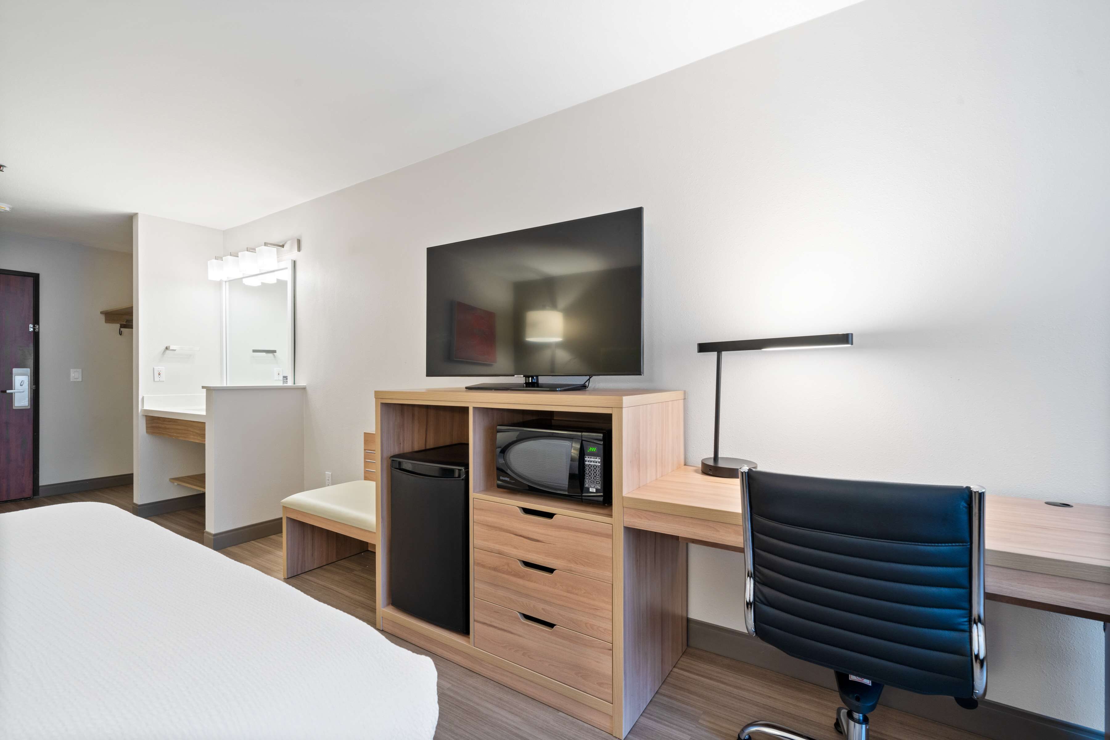 Et moderne hotelværelse med seng, skrivebord med computer, mikroovn, stol og fjernsyn.