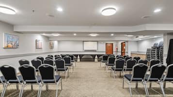 Una sala conferenze con file di sedie nere, uno schermo per proiettore e pavimento rivestito di moquette.