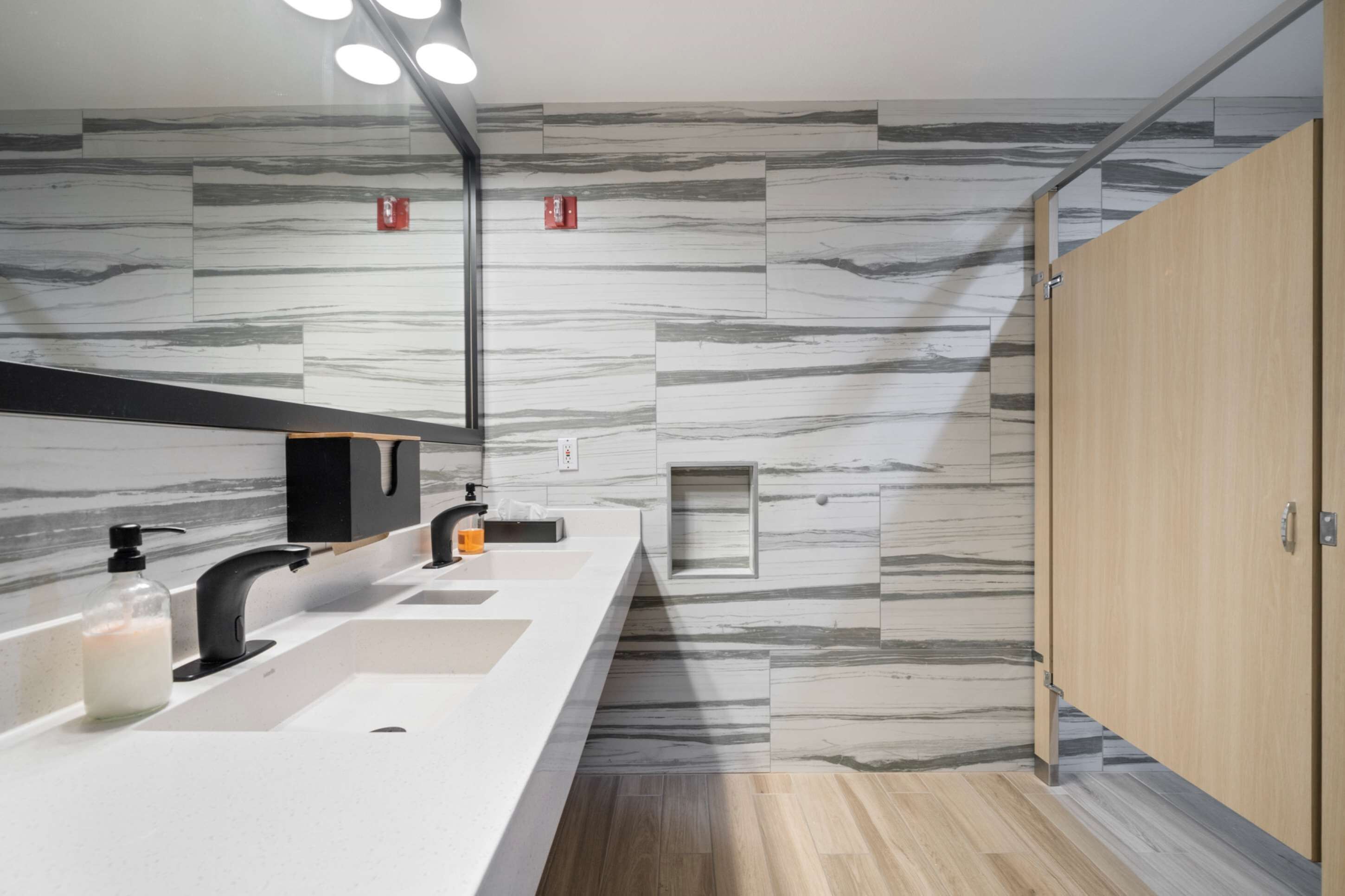 Un baño moderno con pared de diseño de mármol, grifo negro y mueble de madera.