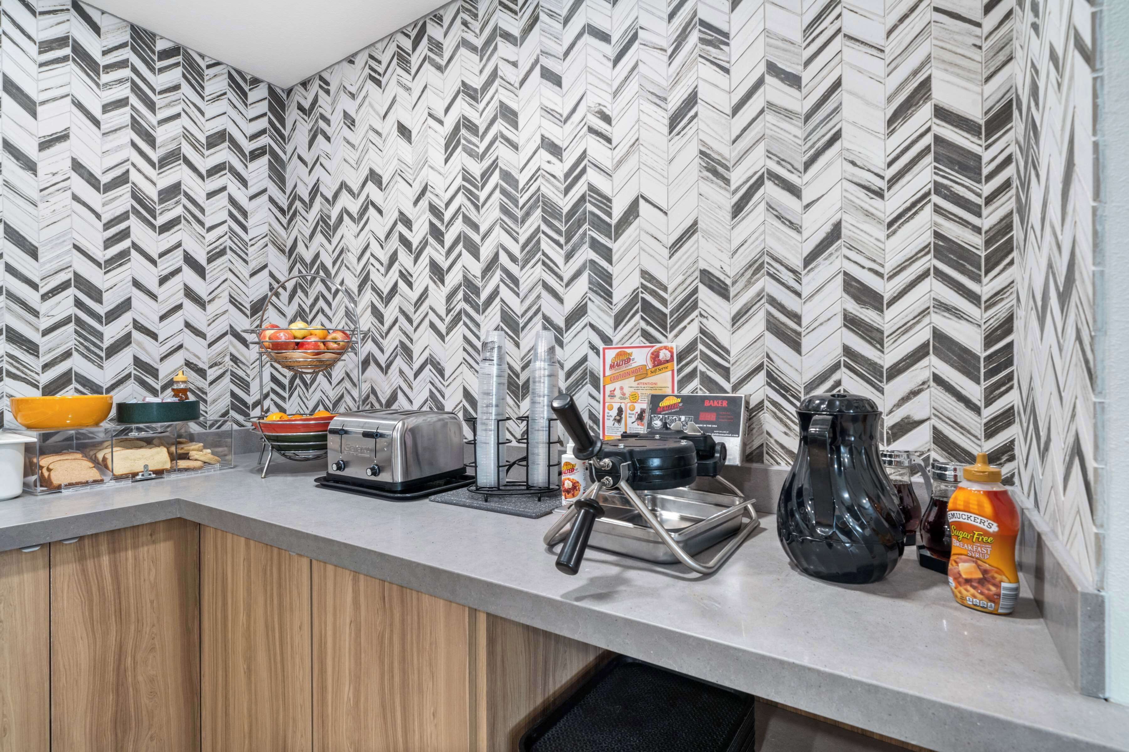 Uma cozinha moderna com um painel de backsplash em padrão losango, uma torradeira, uma cafeteira e uma garrafa de xarope sem açúcar.